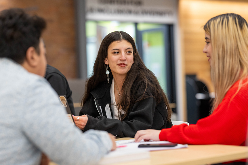 Students gathered around a table talking on campus. 